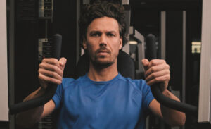 Ein Mann sitzt auf einer Maschine im Fitnessstudio und trainiert seine Muskeln.