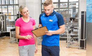 Ein Mann und eine Frau im Fitnessstudio, die auf einem Tablet miteinander sprechen.