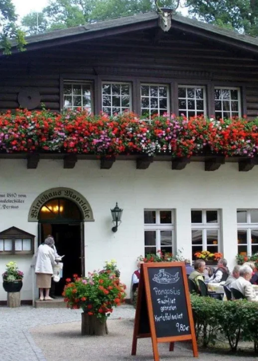 Das Restaurant Wirtshaus Moorlake Restaurant mit bunten Blumen auf dem Balkon, das eine einladende Atmosphäre schafft.