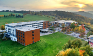 Luftaufnahme des Hotel Wolkenstein mit modernem mehrstöckigem Gebäude, umgeben von grünen Wiesen und herbstlich gefärbten Bäumen bei Sonnenuntergang