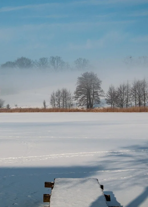 Eine Bank steht auf einem verschneiten Feld mit einem See im Hintergrund.