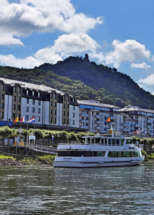 Ein Boot navigiert den Fluss, mit Bergen, die die Landschaft im Hintergrund prägen.