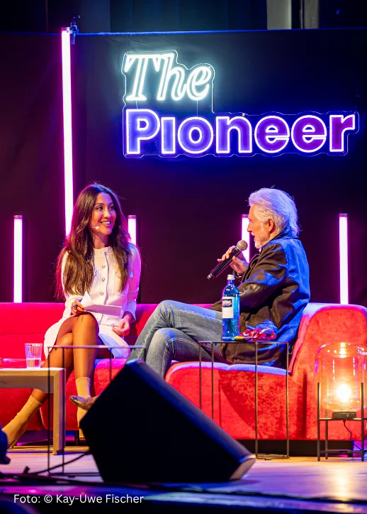 Mann und Frau auf rotem Sofa, während sie im Interview zur Pioneer Celebration Demokracy sprechen.