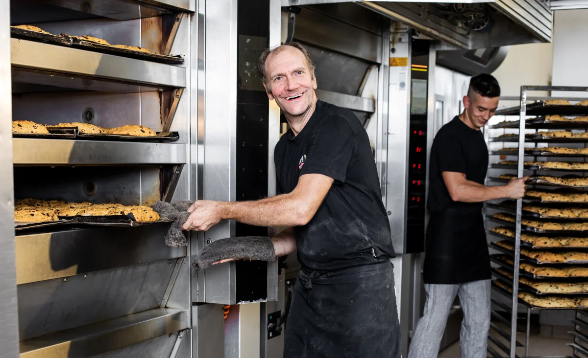 Ein Mann in schwarzem Shirt und schwarzem Schürze hält ein Tablett mit Stollen in der Stollenbäckerei Krause in Dresden.