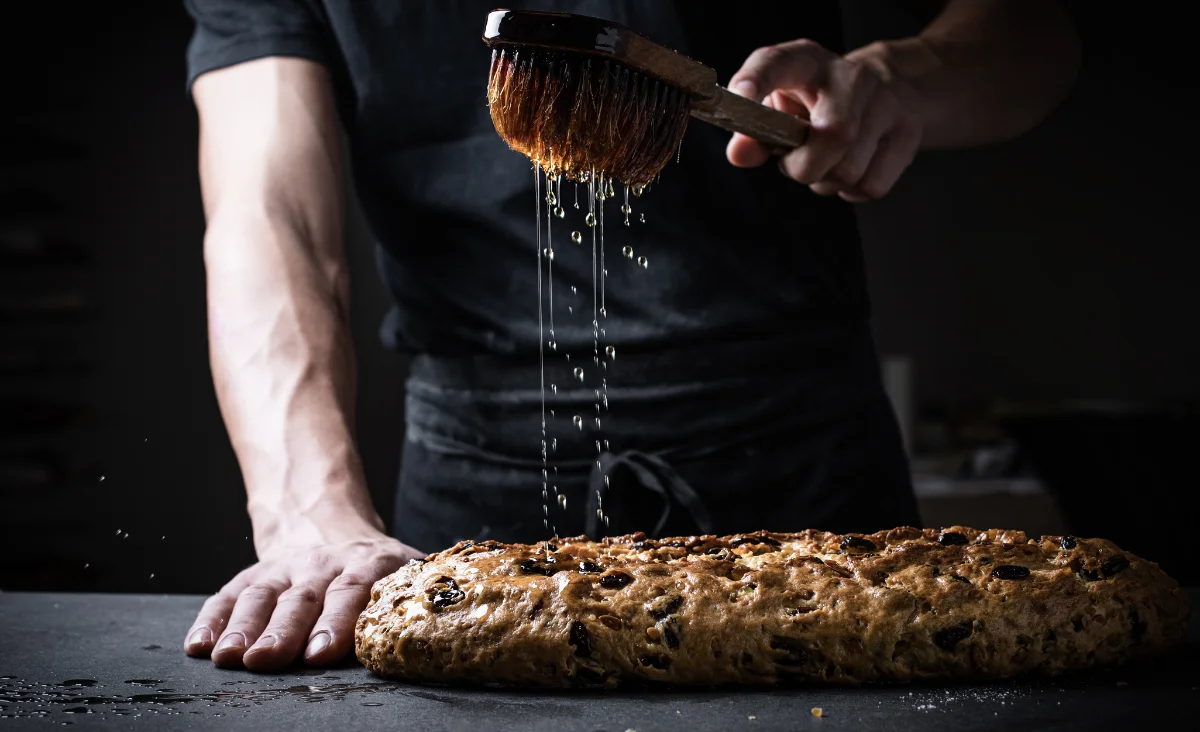 Eine Person bestreut einen Kuchen mit einem Pinsel in der Stollenbäckerei Krause in Dresden.