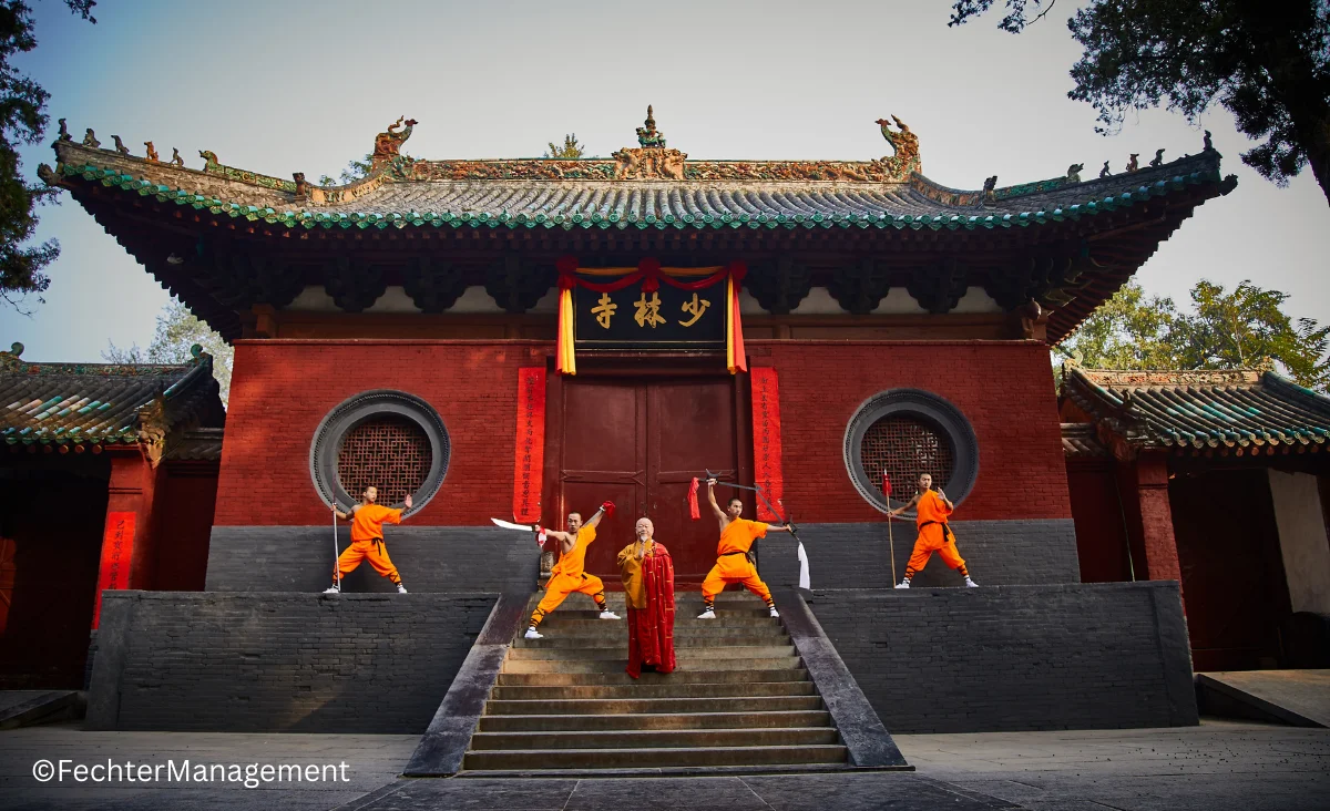 Mönche in orangen Gewändern stehen vor einem chinesischen Tempel.