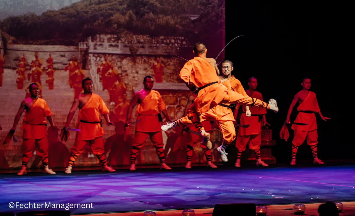 Ein Mann in Orange tritt in einen Kampf gegen einen Mönch ein, die Szene strahlt Dynamik und Intensität aus.