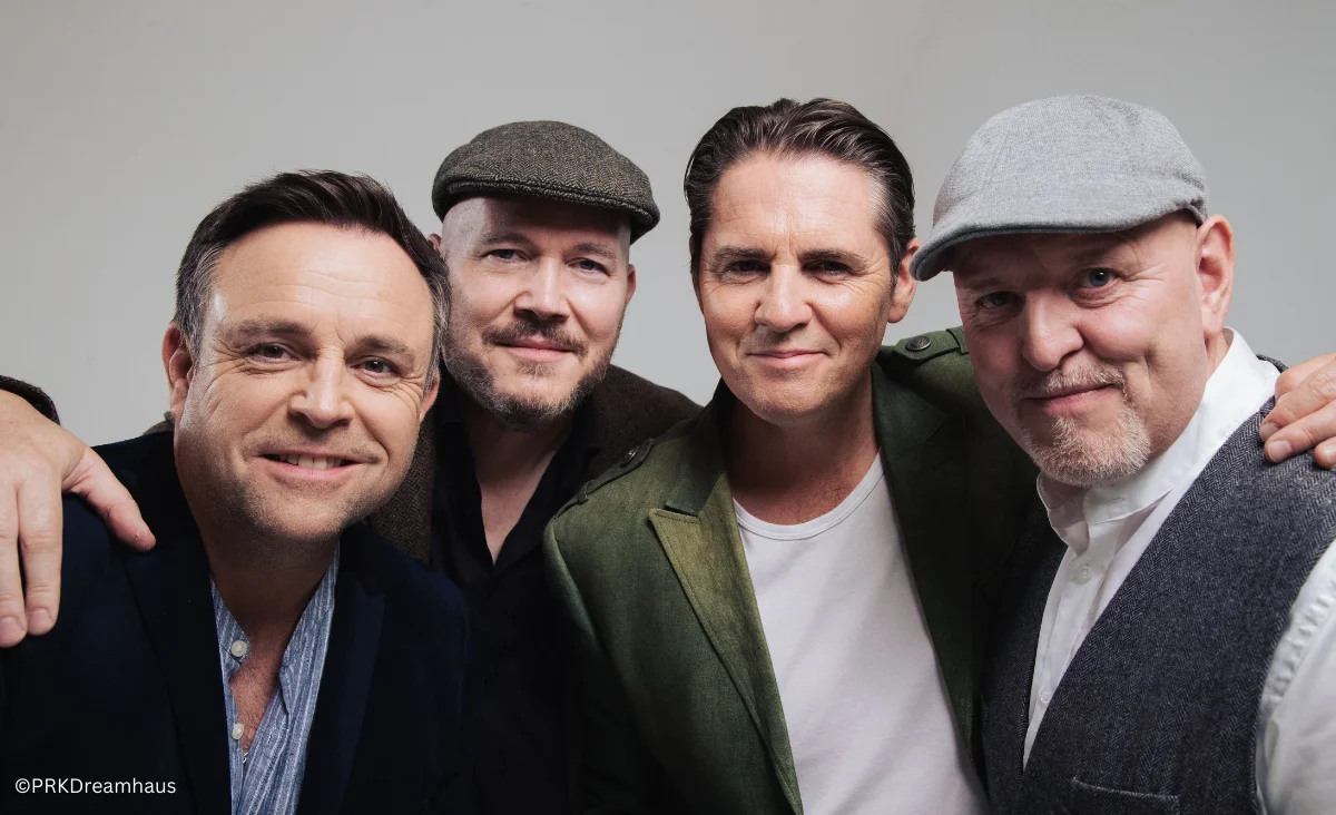 Vier Männer zeigen sich lächelnd in einer gemeinsamen Fotopose.