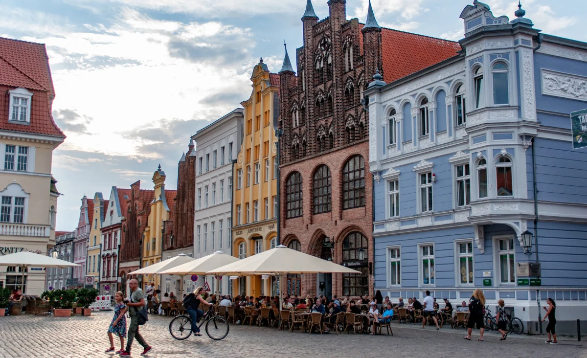 Menschen schlendern über die gepflasterten Straßen einer Stadt auf einer der deutschen Ostseeinseln, umgeben von historischen Gebäuden.