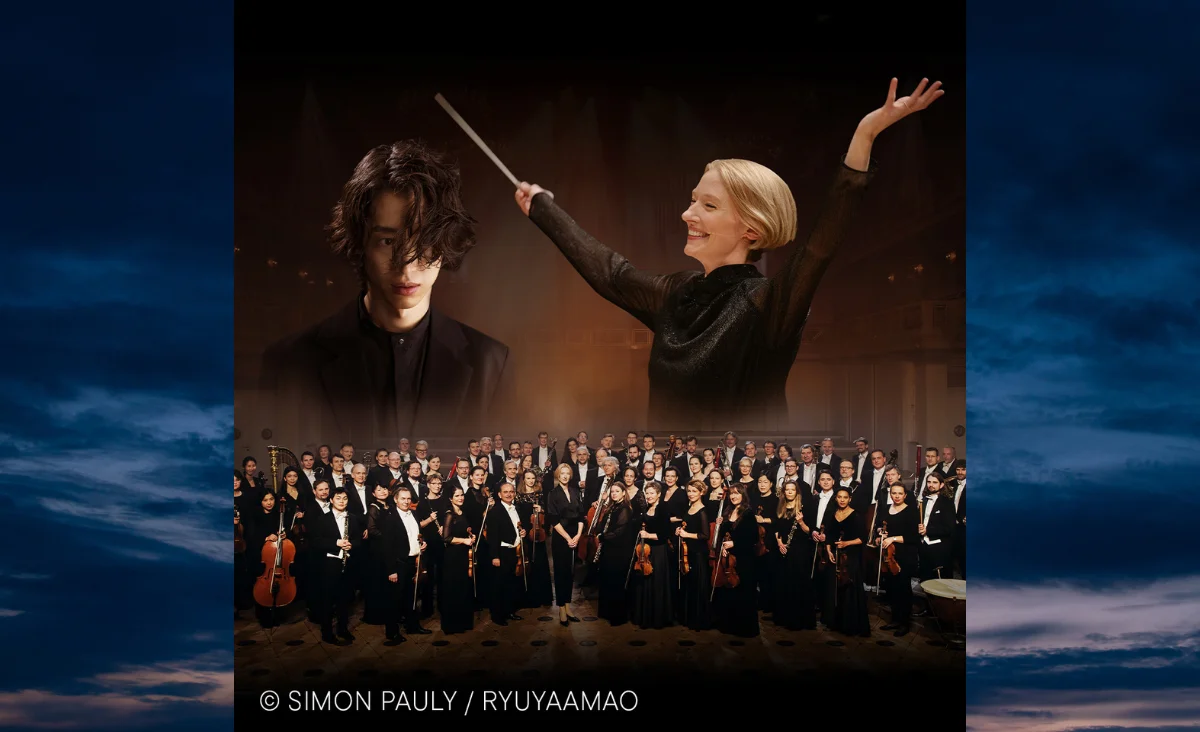 Dirigentin mit erhobenen Armen vor großem Orchester in Konzertsaal