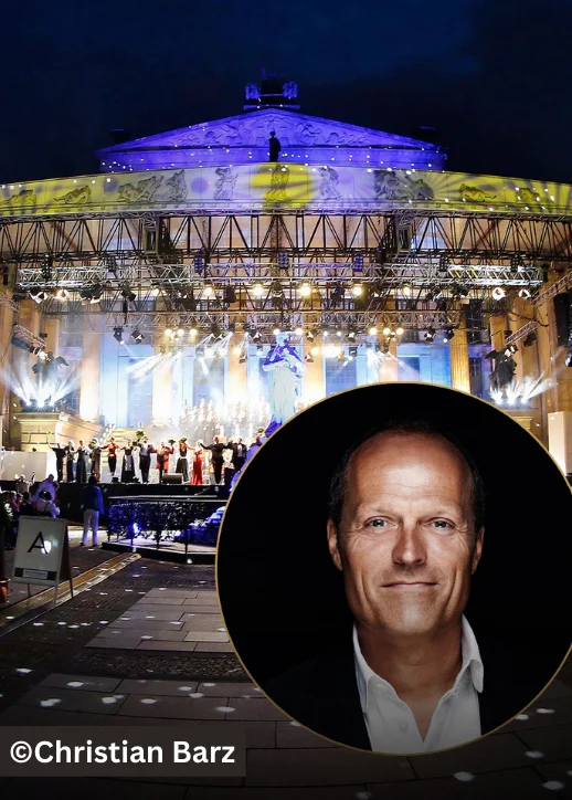 Bühnenaufnahme eines klassischen Open-Air-Konzerts mit einem Chor und einem Flügel im Hintergrund, davor ein Porträt eines Mannes mit offenem Hemdkragen.