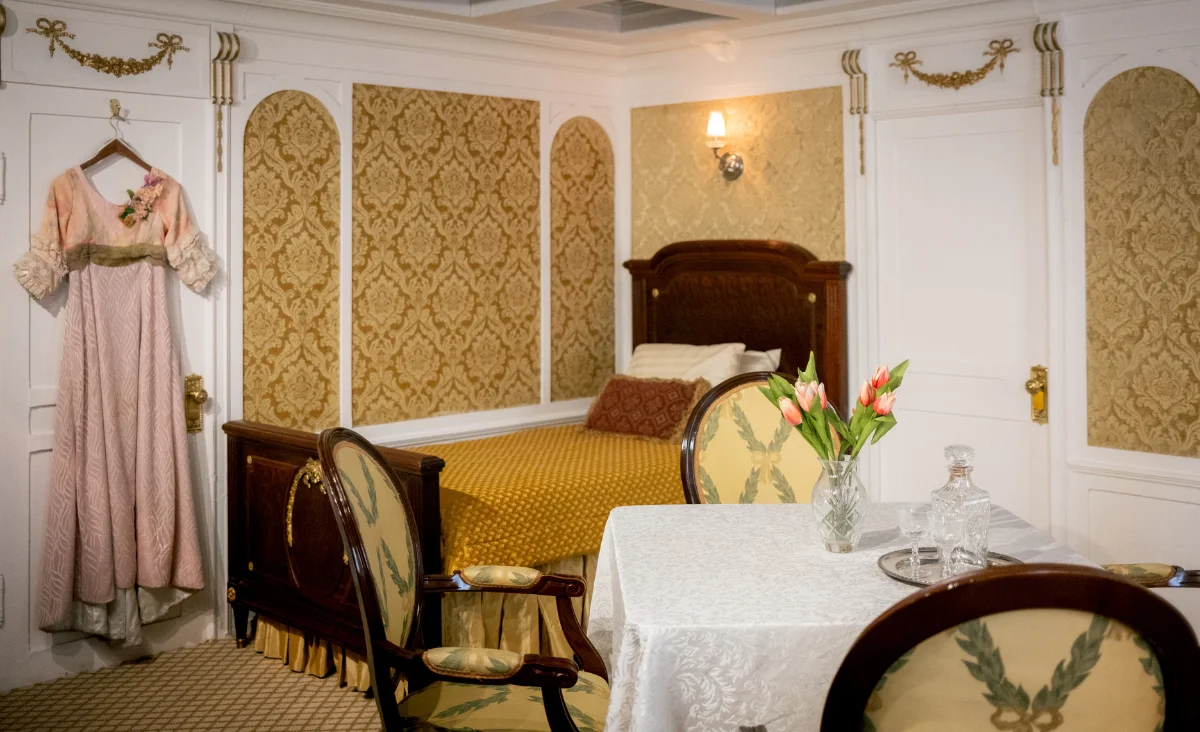 Ein Raum mit einem Bett, einem Tisch und einer Kleid, Teil der Ausstellung "Titanic - Die Ausstellung".