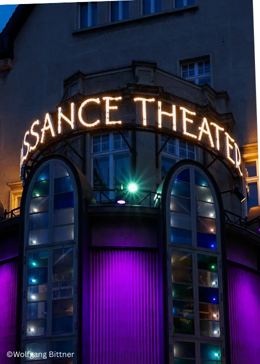 Eingang des Renaissance Theaters Berlin mit beleuchtetem Schriftzug und violett beleuchteten Fenstern in einem historischen Gebäude bei Dämmerung.