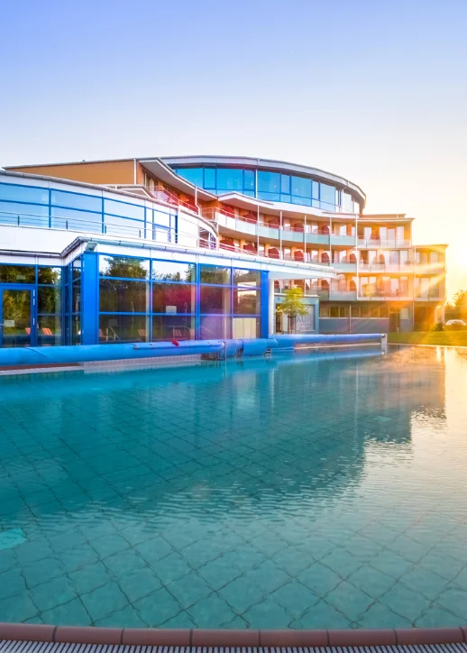 Modernes Kurzentrum mit geschwungener Fassade und großem Außenpool bei Sonnenuntergang