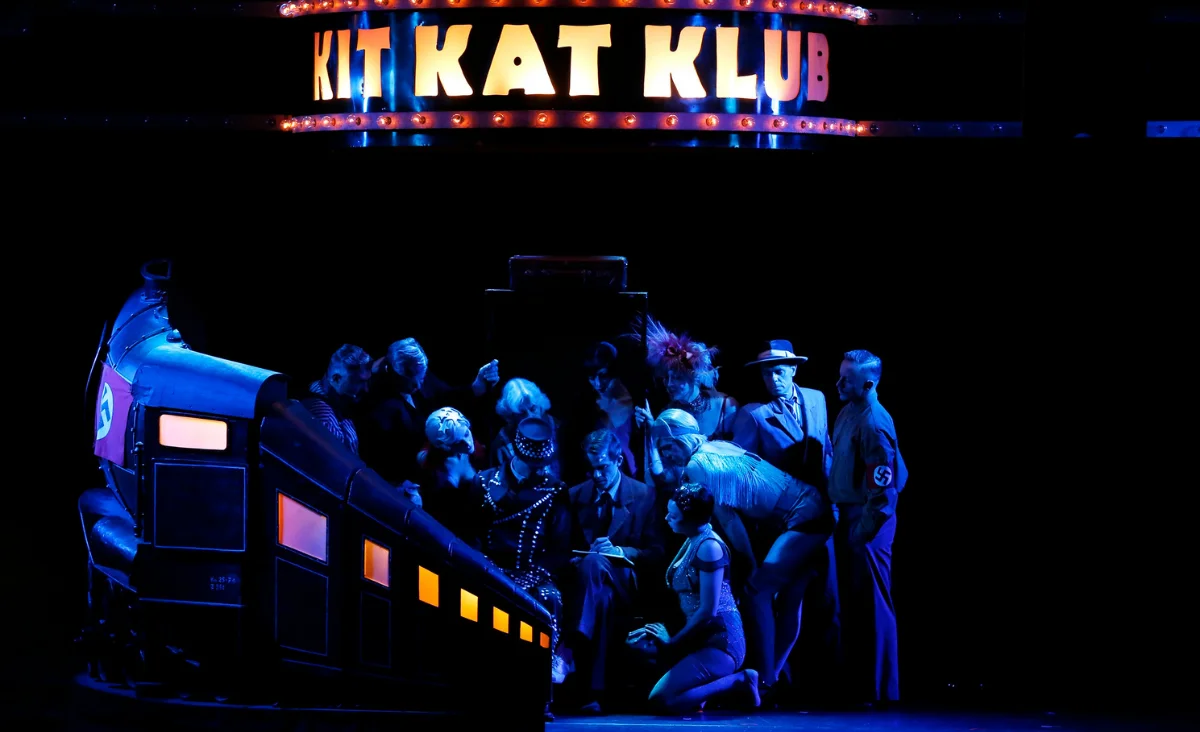Eine lebendige Theateraufführung im Kit Kat Klub mit Darstellern in historischen Kostümen und einer beeindruckenden Bühnenkulisse.
