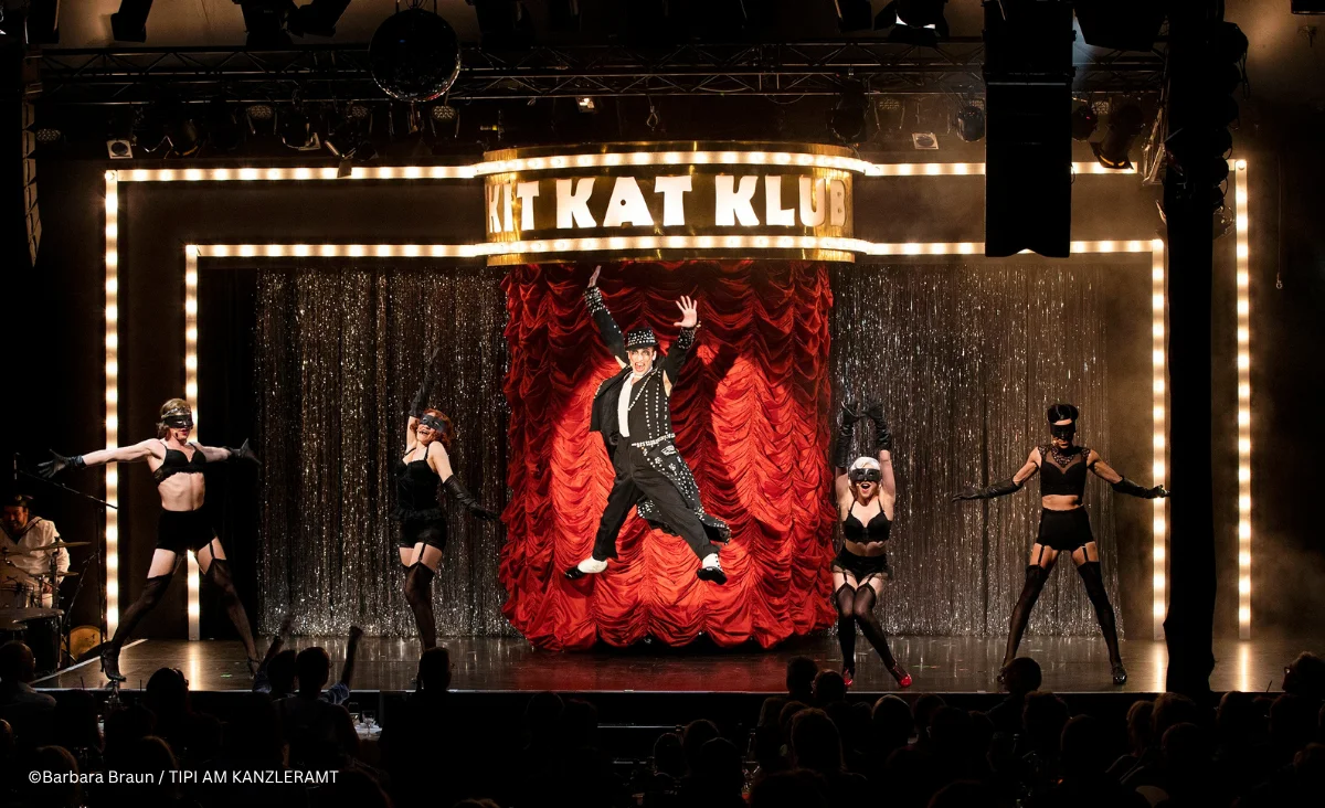 Bühnenbild aus »Cabaret Berlin! – das Berlin Musical« mit beleuchtetem Schriftzug »KIT KAT KLUB« über einer glitzernden Vorhangkulisse. Die Szene ist von warmem Scheinwerferlicht und Lichterrahmen eingefasst.