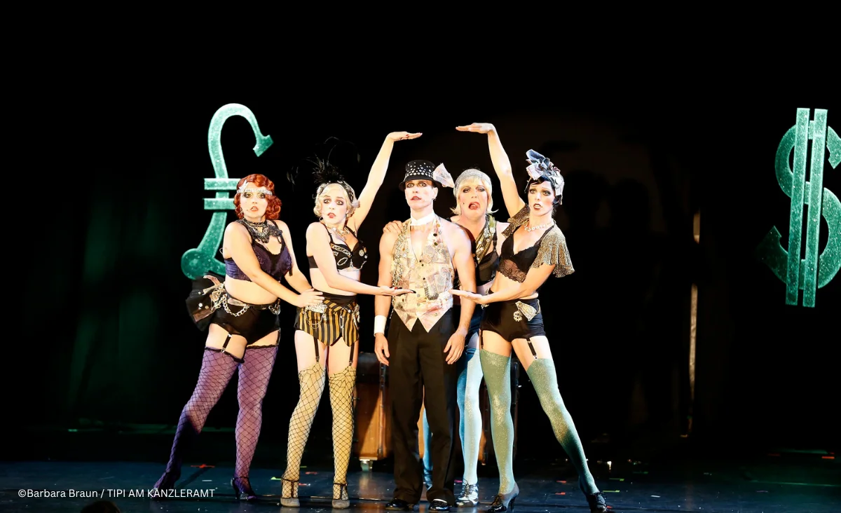 Bühnenbild aus »Cabaret Berlin! – das Berlin Musical« mit sechs Personen in aufwendigen, burlesken Kostümen. Der Bühnenhintergrund ist dunkel gehalten, wodurch die Kostüme und Symbole besonders hervortreten.