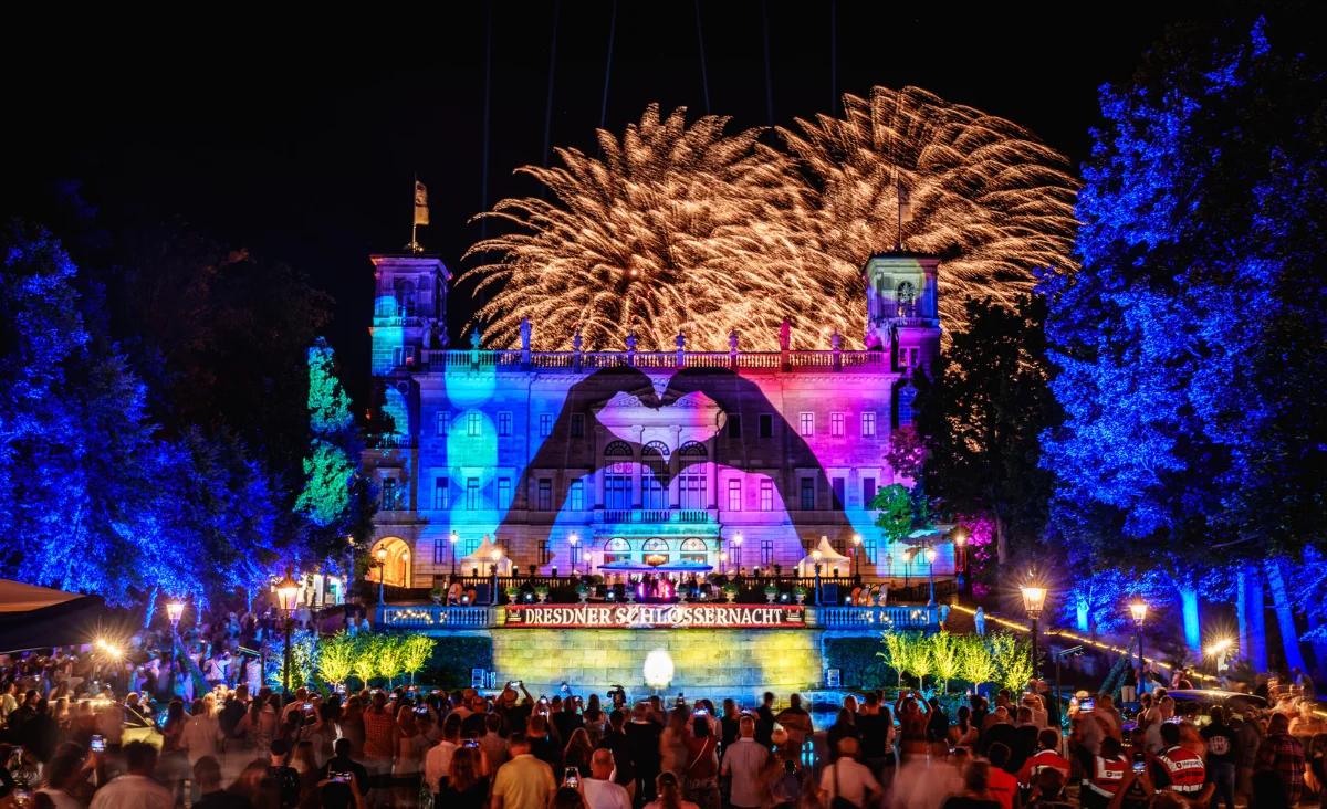 Feuerwerk und Lichtstrahlen über einem historischen Schloss mit beleuchteten Bäumen und einer Menschenmenge bei der Dresdner Schlössernacht.