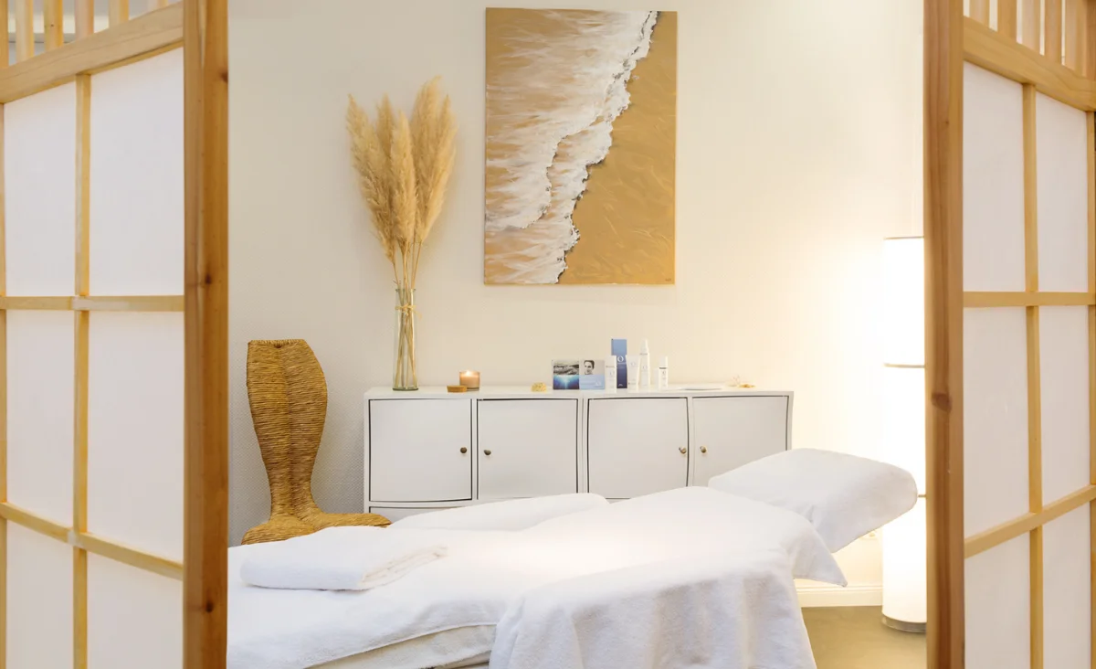 Behandlungsraum im Hotel Kaiserhof Heringsdorf mit Massageliege, weißer Kommode, Wandbild mit Meeresmotiv und dekorativem Pampasgras.