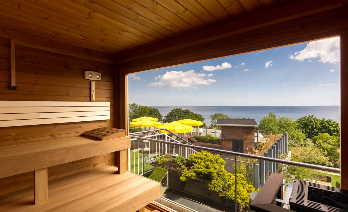 Holzverkleideter Saunaraum mit breiten Sitzbänken und großem Panoramafenster. Durch das Fenster ist eine gepflegte Außenanlage des Hotel Kaiserhof Heringsdorf sichtbar