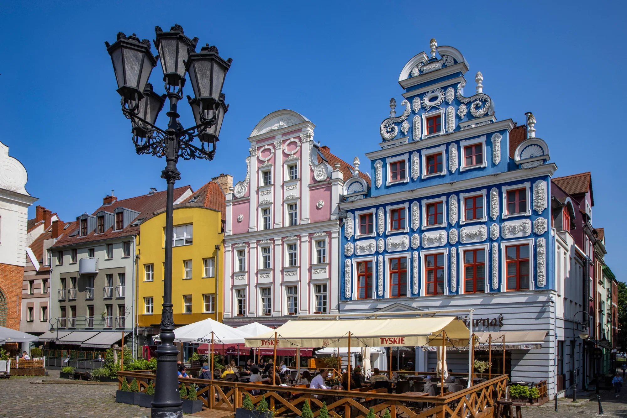 Historische Giebelhäuser in einer Altstadt mit einem Straßencafé und einer dekorativen Laterne im Vordergrund