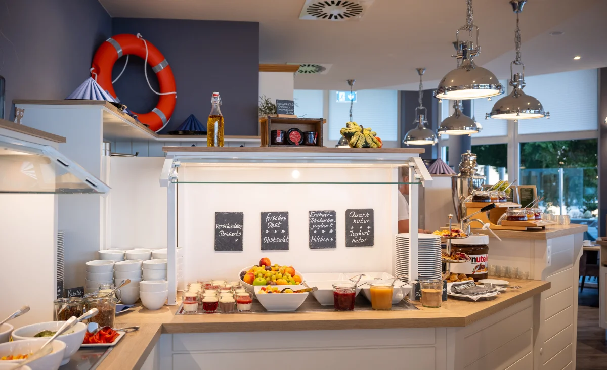 Buffetbereich mit Obstschale, Gläsern, Tellern und dekorativen Tafeln in modernem Aparthotel-Interieur