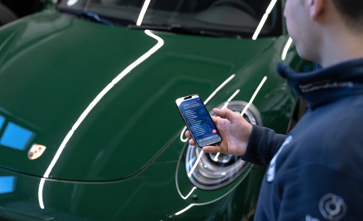 Nahaufnahme einer Hand, die mit einem Poliergerät die Motorhaube eines grünen Fahrzeugs mit Porsche-Emblem bearbeitet