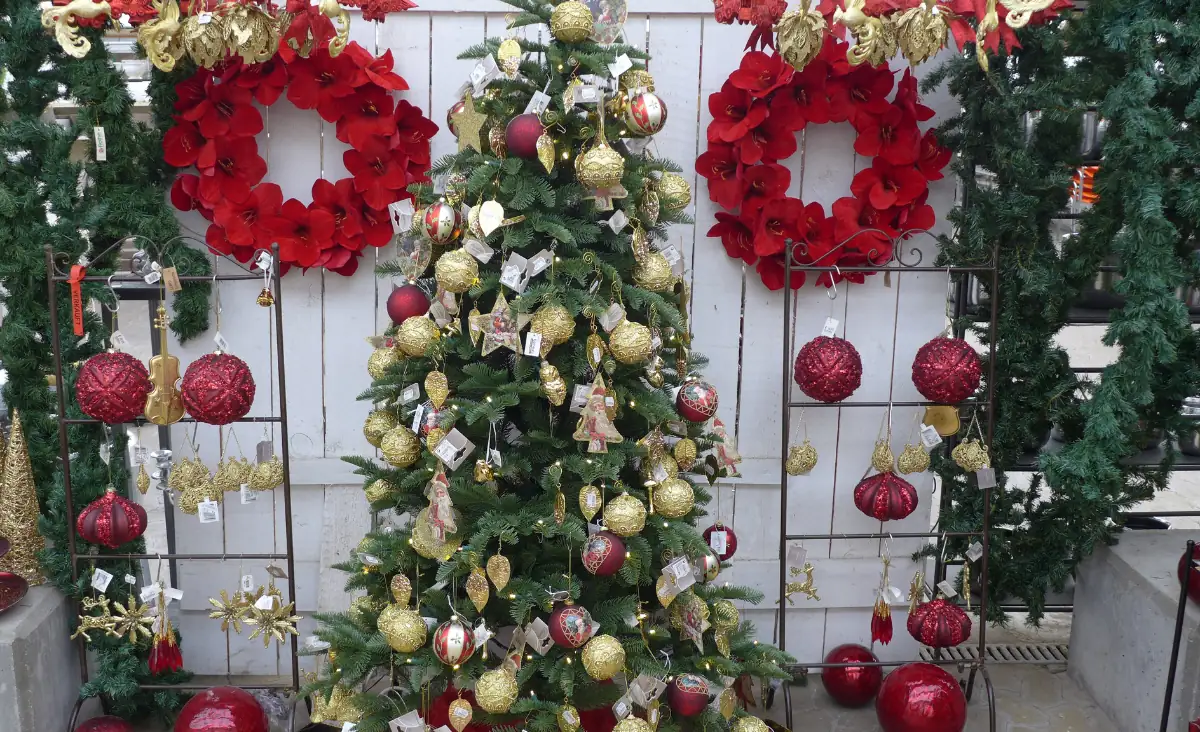 Weihnachtsbaum mit goldenen und roten Kugeln sowie Sternen, umgeben von roten Weihnachtskränzen und weiteren Dekorationen in einem Gartenbaugeschäft