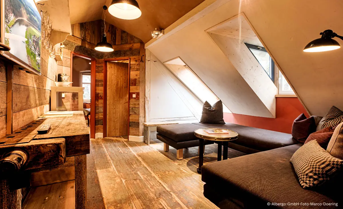 Gemütlicher Hotelzimmerbereich mit Holzboden, zwei Sofas, einem runden Tisch und Dachfenstern im Winterdorf Schmilka Hotel Zur Mühle