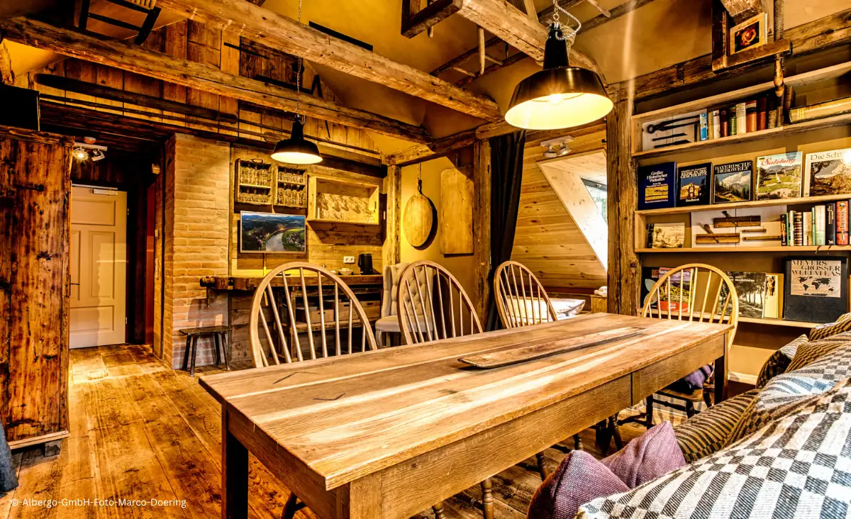 Rustikaler Gastraum im Winterdorf Schmilka Hotel Zur Mühle mit Holztisch, Stühlen, sichtbaren Holzbalken und Bücherregal an der Wand